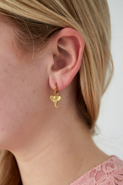 Close-up of a woman wearing gold plated elephant charm hoop earring with light blonde hair and pink lace top
