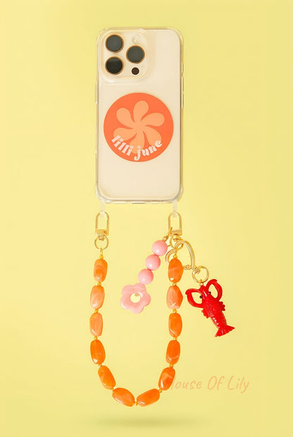 Clear phone case with orange and pink beaded straps and a red lobster charm with gold heart clip hanging against a yellow background