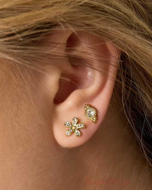 Close-up of woman’s ear showing gold-toned crystal stud and floral stud earrings