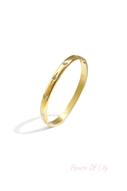 Gold-tone slim metal bangle bracelet with crystal star and crescent accents on white background