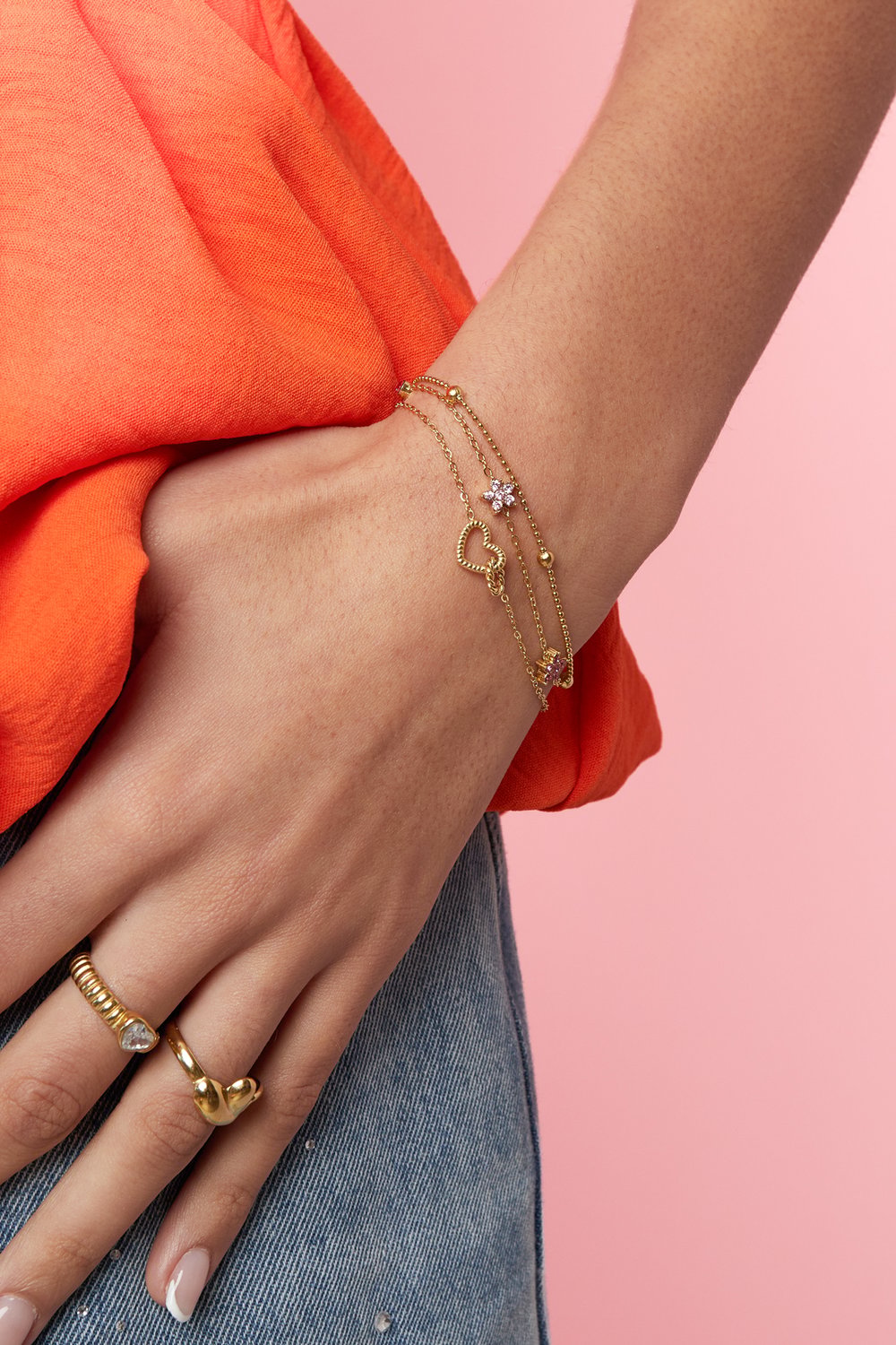 Delicate gold multi-strand bracelet featuring a sculpted heart, flower charm, and beads, worn on a model's wrist.
