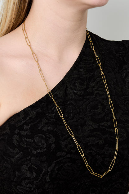 Close-up of gold elongated link chain necklace worn on a woman with black textured top
