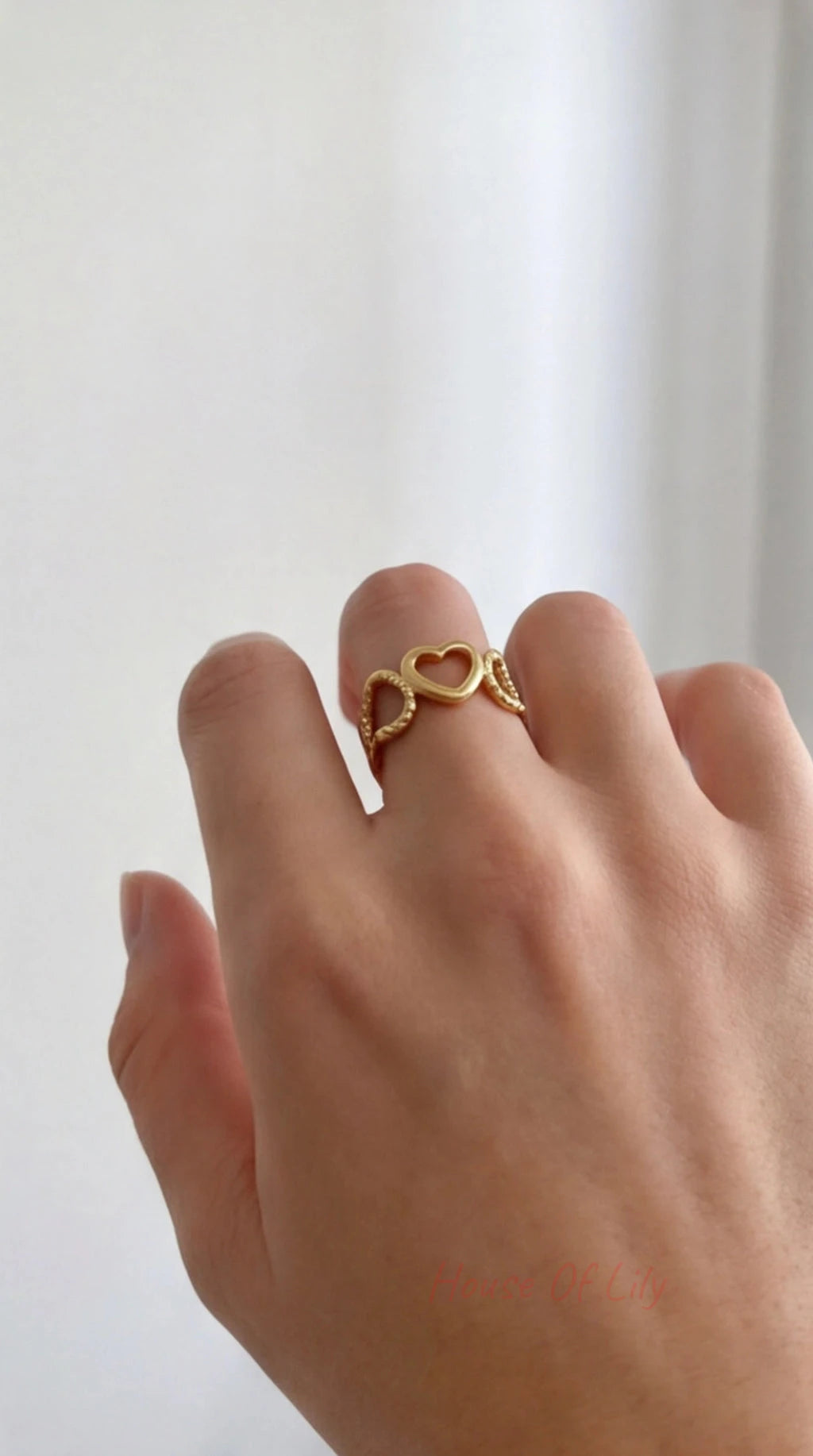 Gold heart-shaped ring on a person's finger against a white background