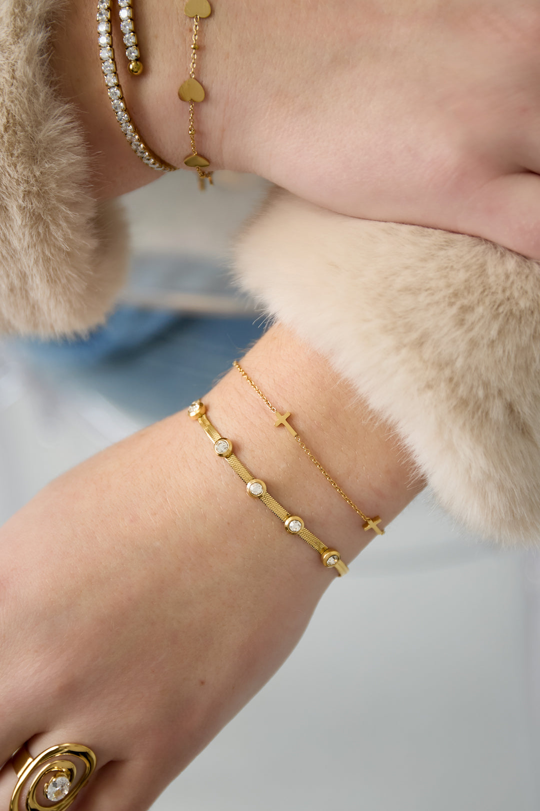 Close-up photo of a wrist wearing the gold rhinestone chain bracelet paired with other delicate gold bracelets and a fur cuff