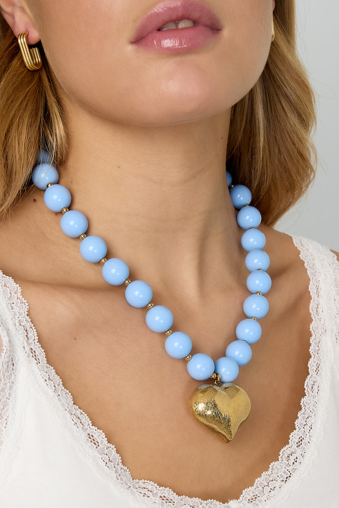 Close-up of model's neck showing baby blue chunky bead necklace with gold heart pendant