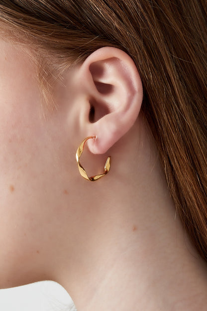 Close-up of gold twisted hoop clip earring worn on a woman’s ear highlighting the modern design