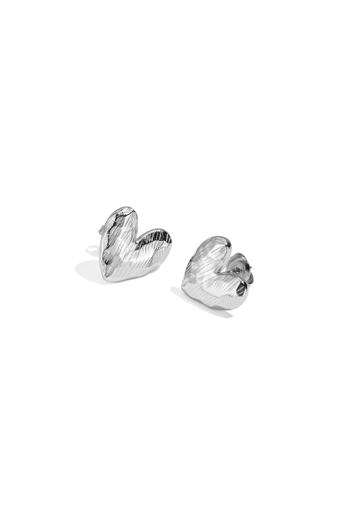 Close-up of silver heart-shaped stud earrings with textured finish photographed on white background