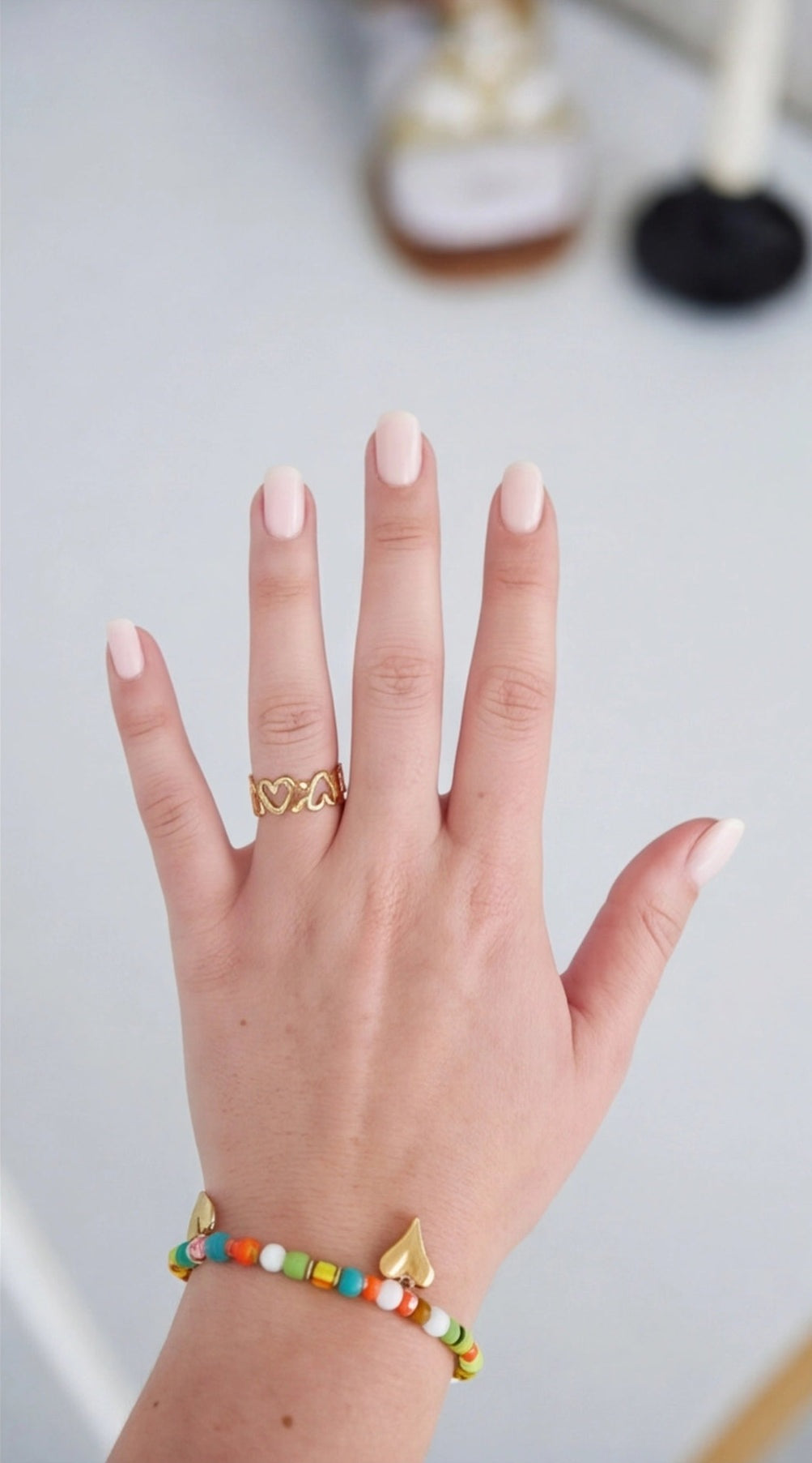 Hand wearing a gold ring with a colorful beaded bracelet on a light background