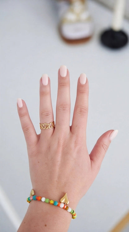 Hand wearing a gold ring with a colorful beaded bracelet on a light background