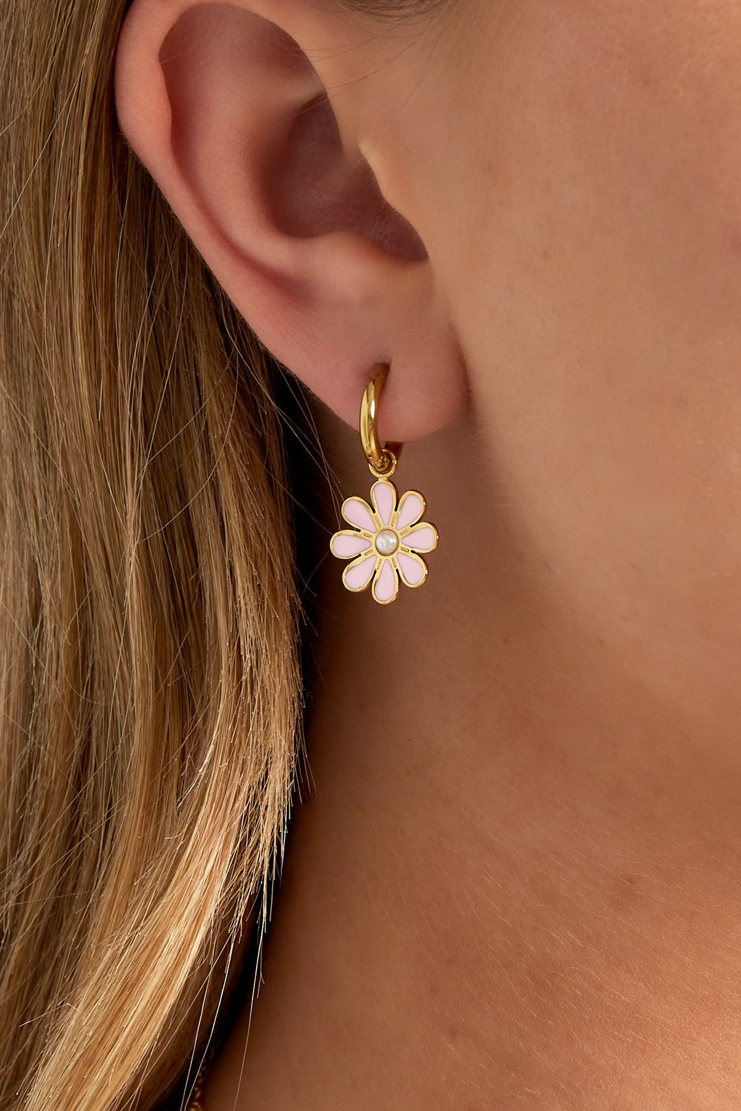 Close-up of gold hoop earring with pink enamel flower charm and pearl center worn by woman