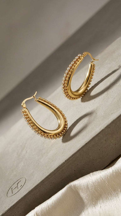 Gold Drip Drop Glow hoop earrings featuring a beaded edge and a row of embedded crystals on a concrete surface.