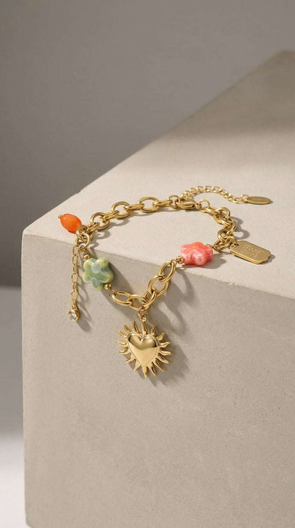 Charm Era Unlocked gold-tone chain bracelet with heart-sun charm, pastel floral beads, and a "Good Luck" tag.