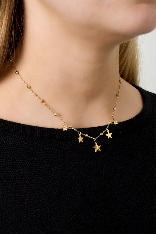 Close-up view of necklace worn on model neck featuring gold star pendants and small beads over a black top