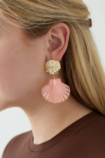 Close-up of pink shell drop earring worn by woman with blonde hair and brown top