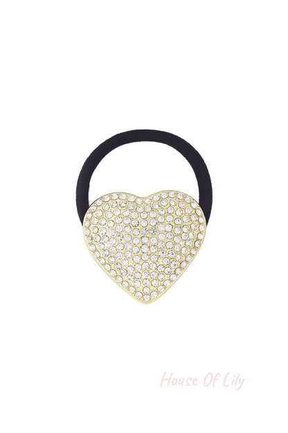 Close-up of a black elastic hair tie featuring a gold-tone heart charm encrusted with clear sparkling crystals