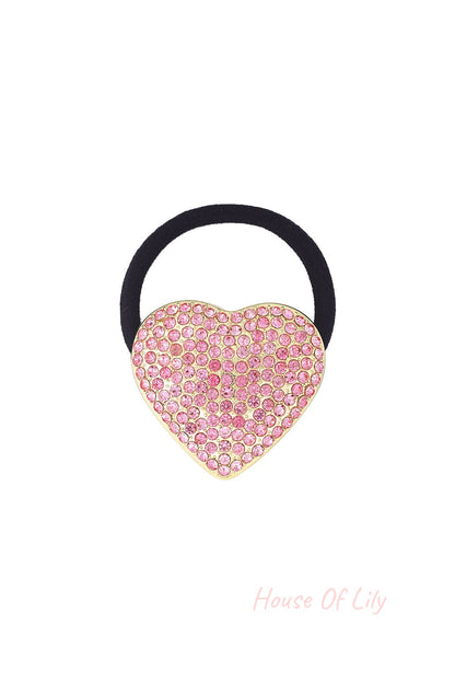 Black elastic hair tie with a gold-tone heart charm encrusted with pink sparkling crystals on a white background