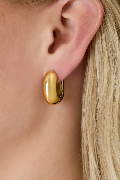 Close-up of gold chunky oval hoop earring worn on a woman's ear highlighting smooth polished design