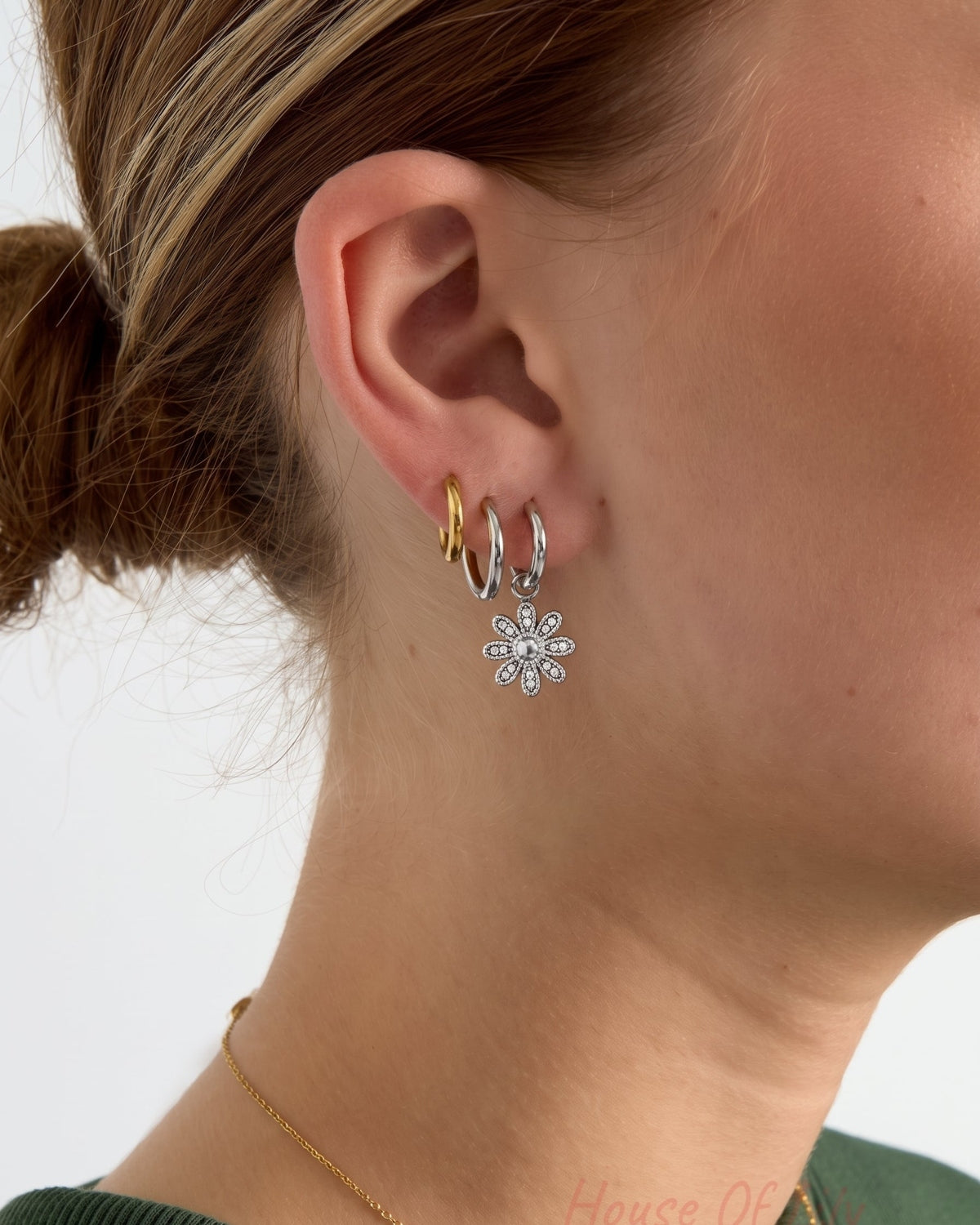 Silver flower drop earring on a hoop, worn on an ear with other hoops.