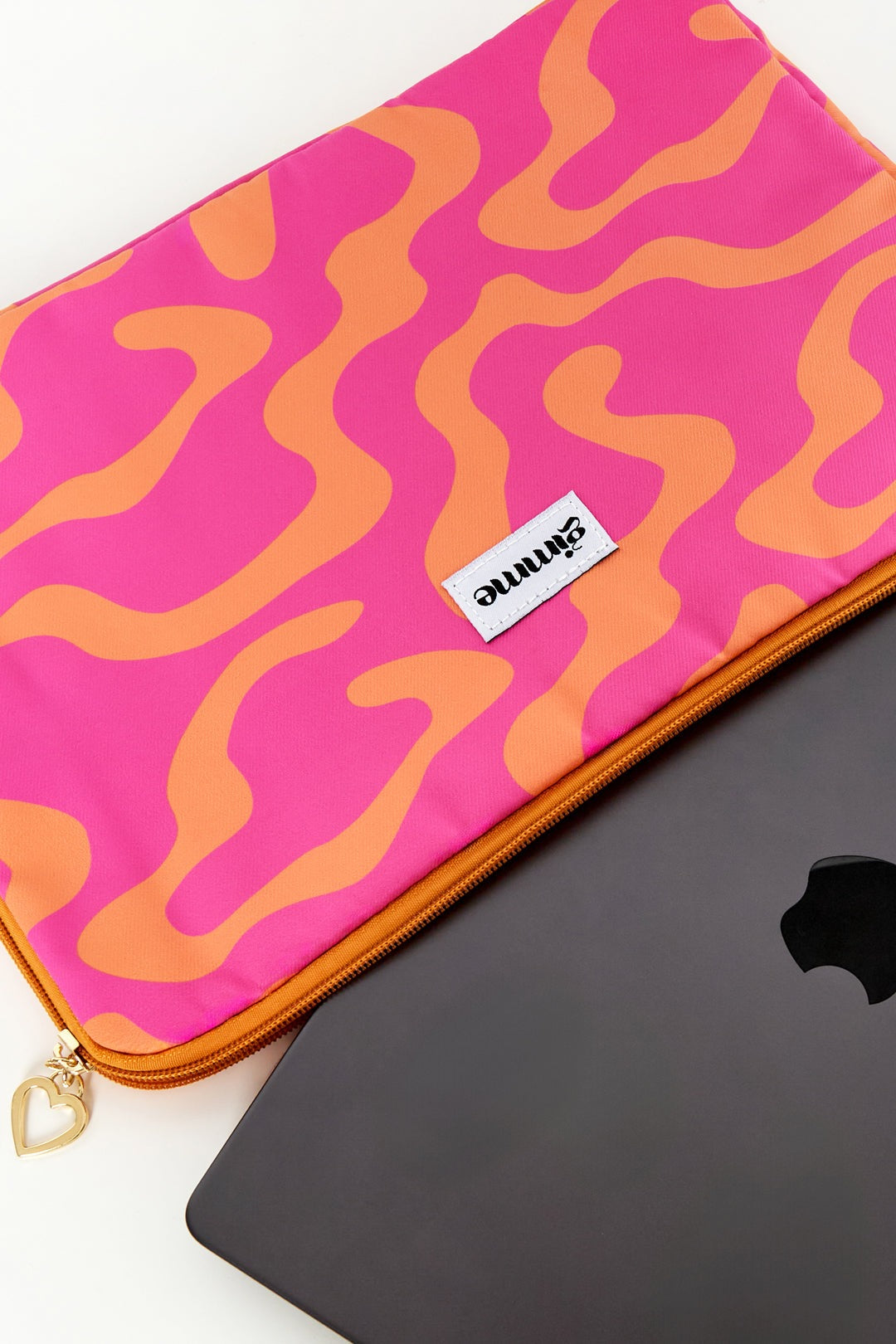 Close-up of pink and orange wavy patterned laptop sleeve partially open showing a black laptop inside, with heart-shaped zipper pull