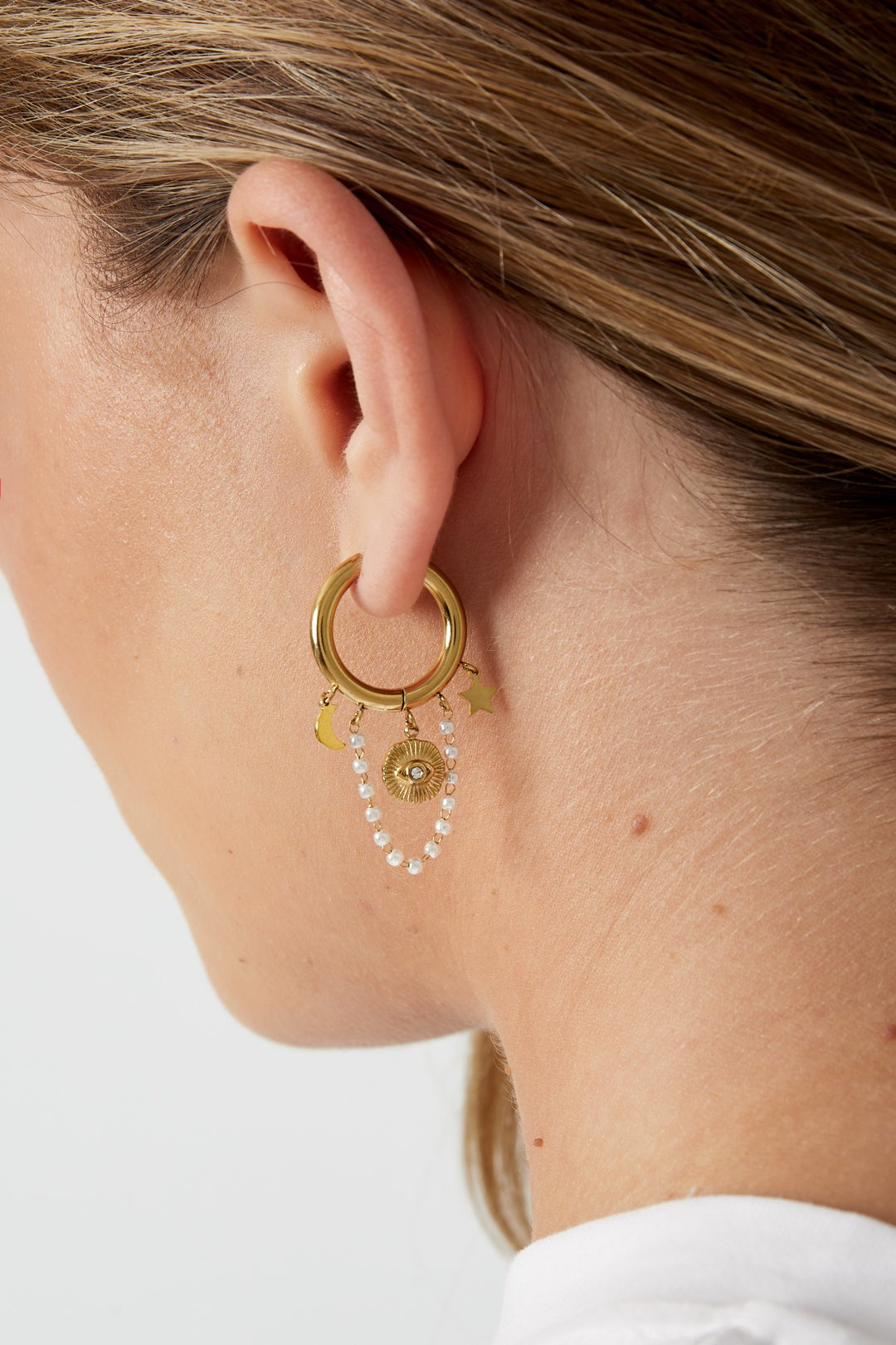 Close-up of a woman wearing gold celestial charm hoop earring featuring star, moon, sun charms and pearl chain
