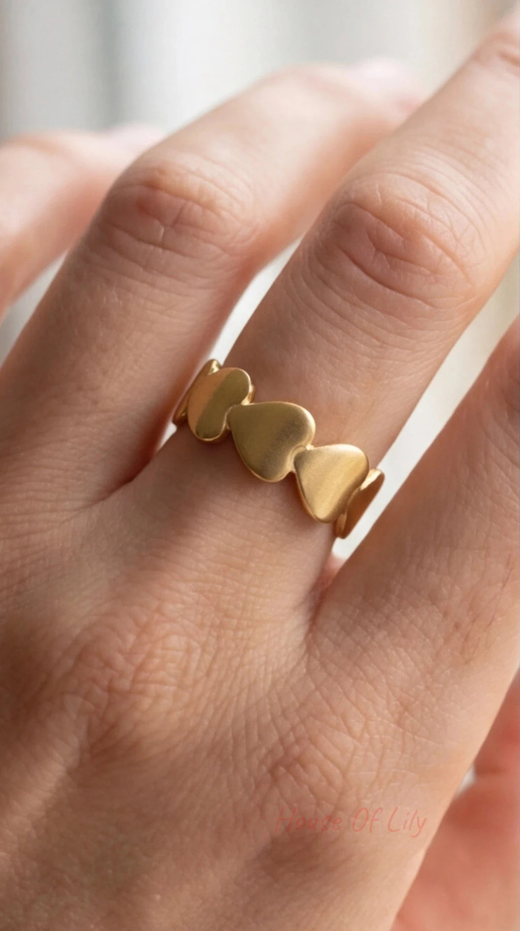 Gold heart-shaped ring on a person's finger with a blurred background