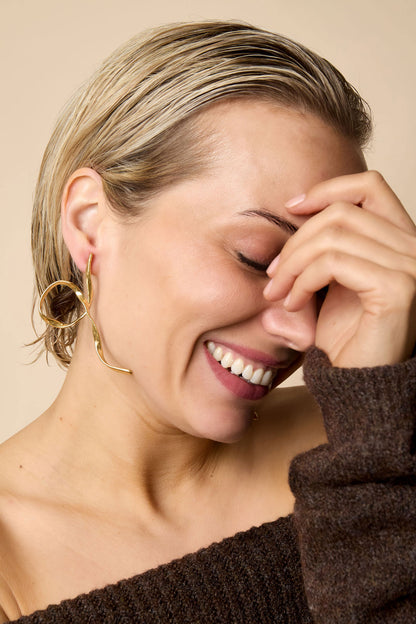 Smiling woman with short blonde hair wearing gold twist loop statement earrings and cozy dark sweater