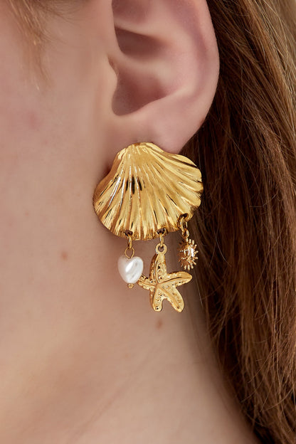 Close-up of seashell charm drop earring worn on woman's ear showing gold shell base and three dangling charms