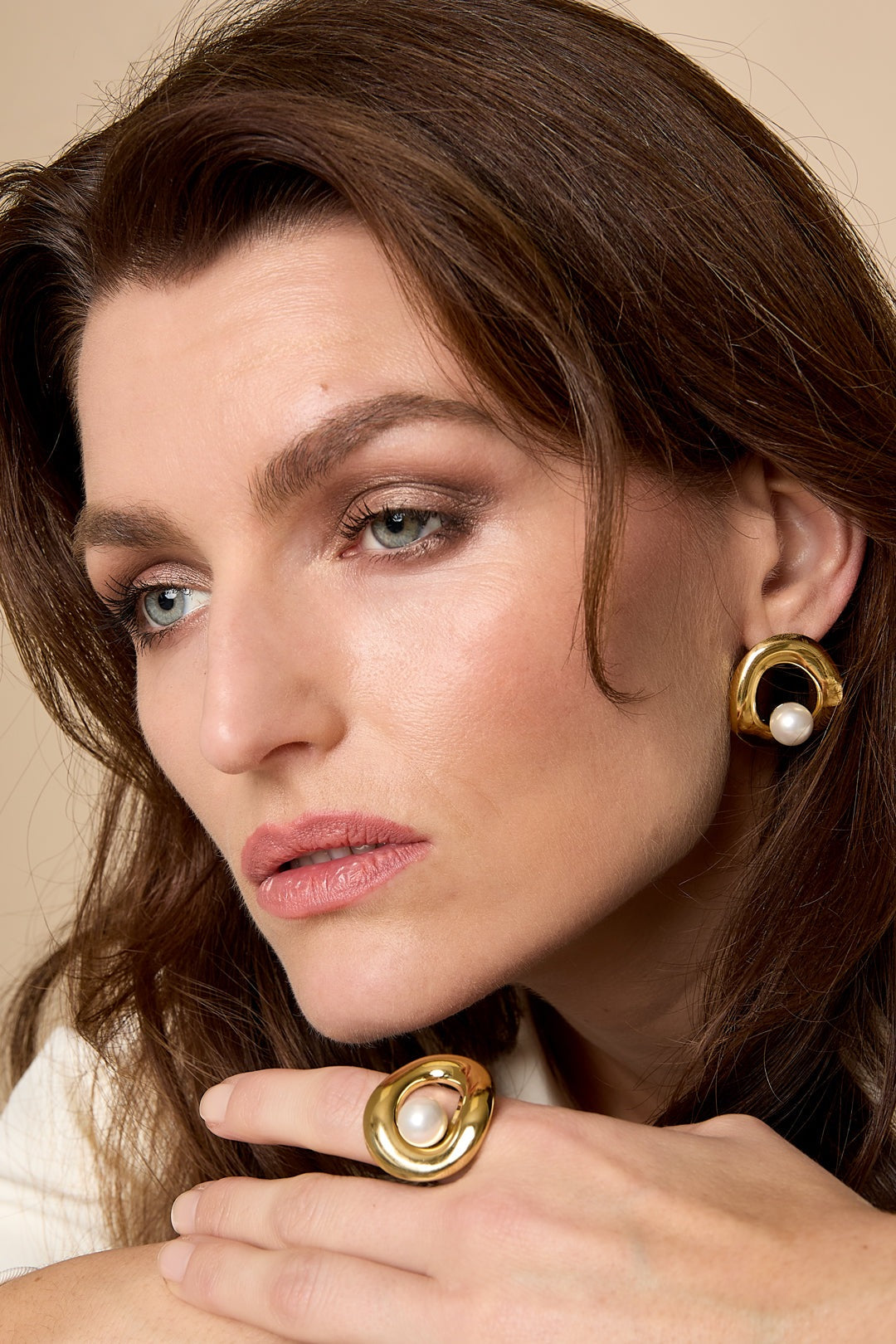 Close-up of woman wearing gold-tone circle pearl stud earrings and matching ring, showcasing youthful boutique style
