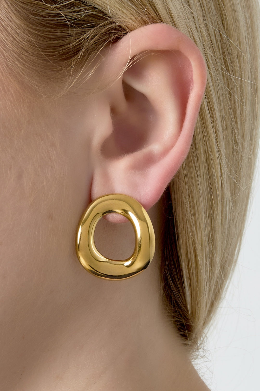 Close-up view of gold irregular hoop earring worn on woman’s ear showcasing lightweight and unique design