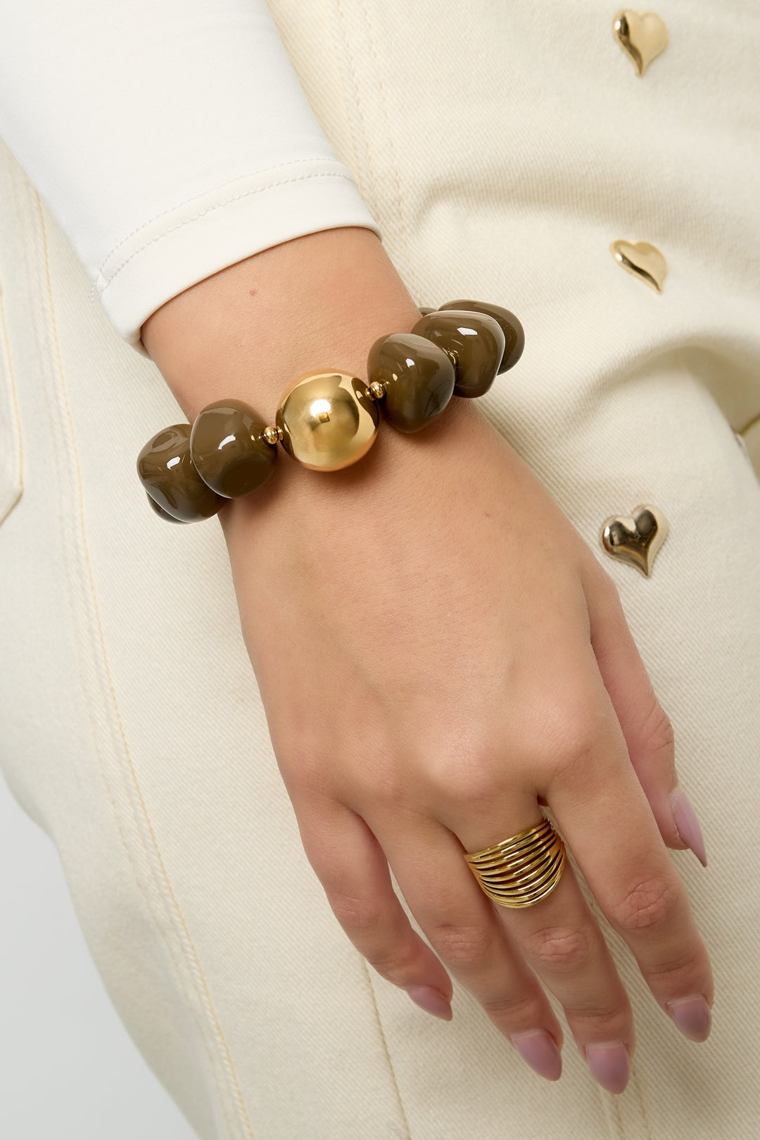 Model wearing chunky brown acrylic beaded bracelet with gold accent, shown on wrist with cream outfit