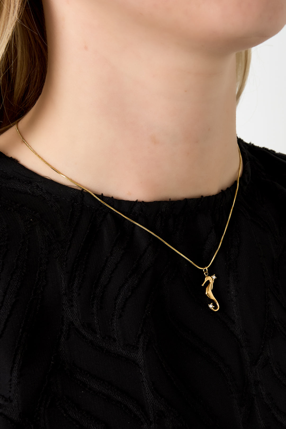 Close-up of gold seahorse pendant necklace worn by a woman in a black textured top