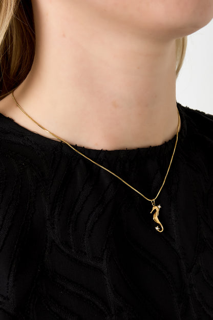 Close-up of gold seahorse pendant necklace worn by a woman in a black textured top