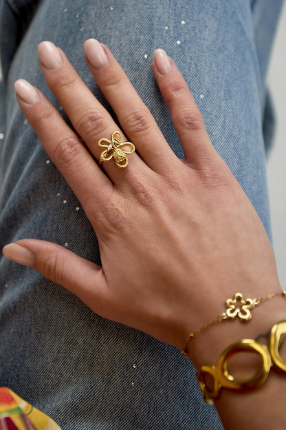 Hand wearing adjustable gold flower loop ring paired with matching bracelet on denim