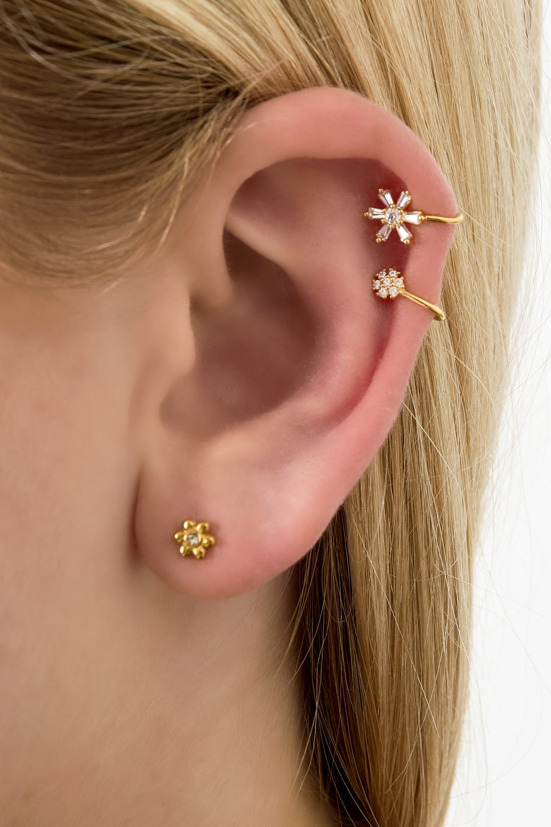 Close-up of ear wearing two gold flower-inspired ear cuffs and a small stud, showcasing intricate crystal details and soft youthful design