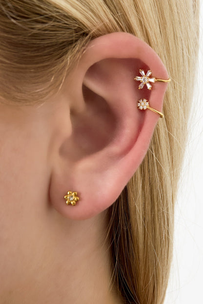Close-up of ear wearing two gold flower-inspired ear cuffs and a small stud, showcasing intricate crystal details and soft youthful design