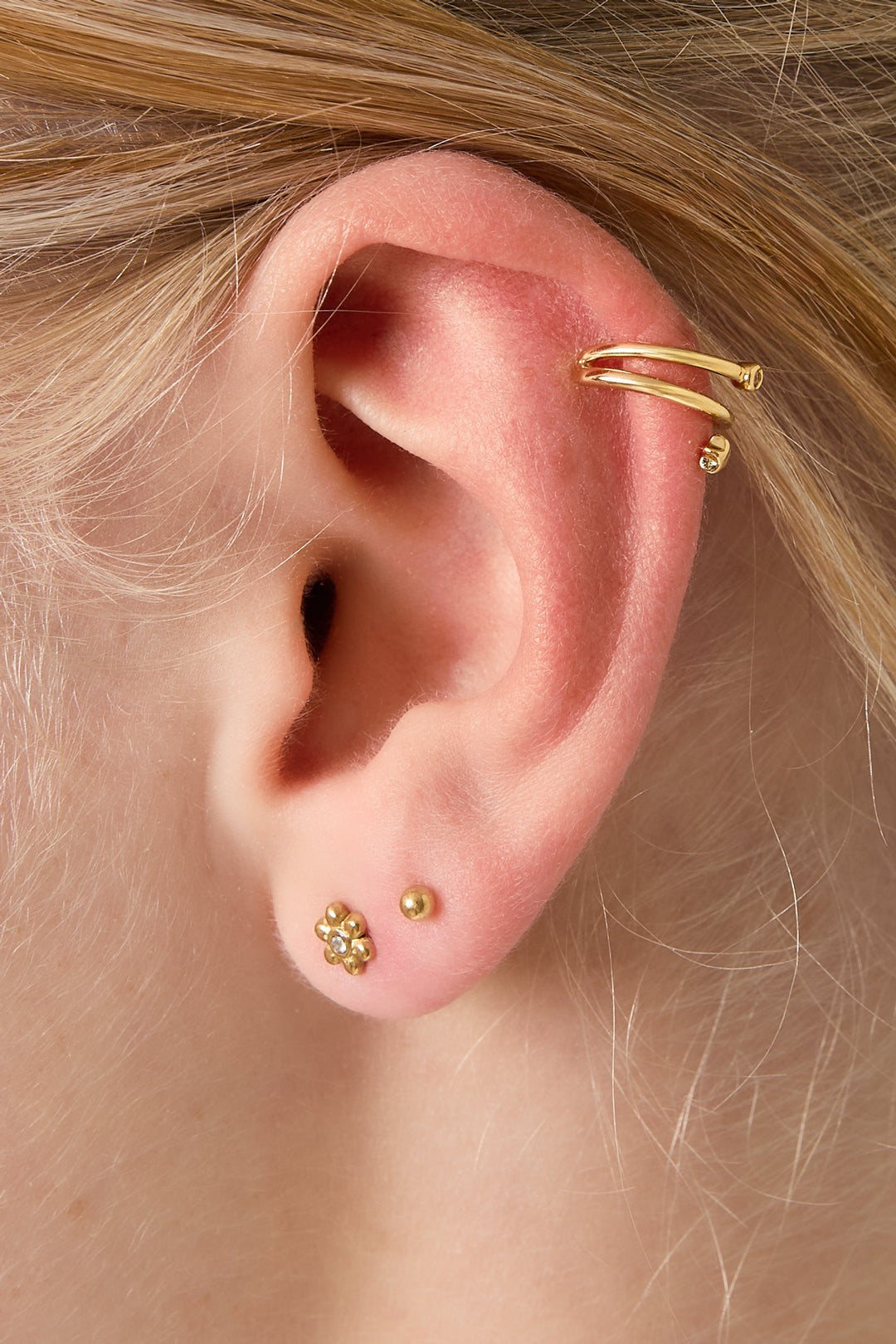 Ear close-up with gold star and rhinestone double spiral ear cuff worn alongside small floral and ball stud earrings