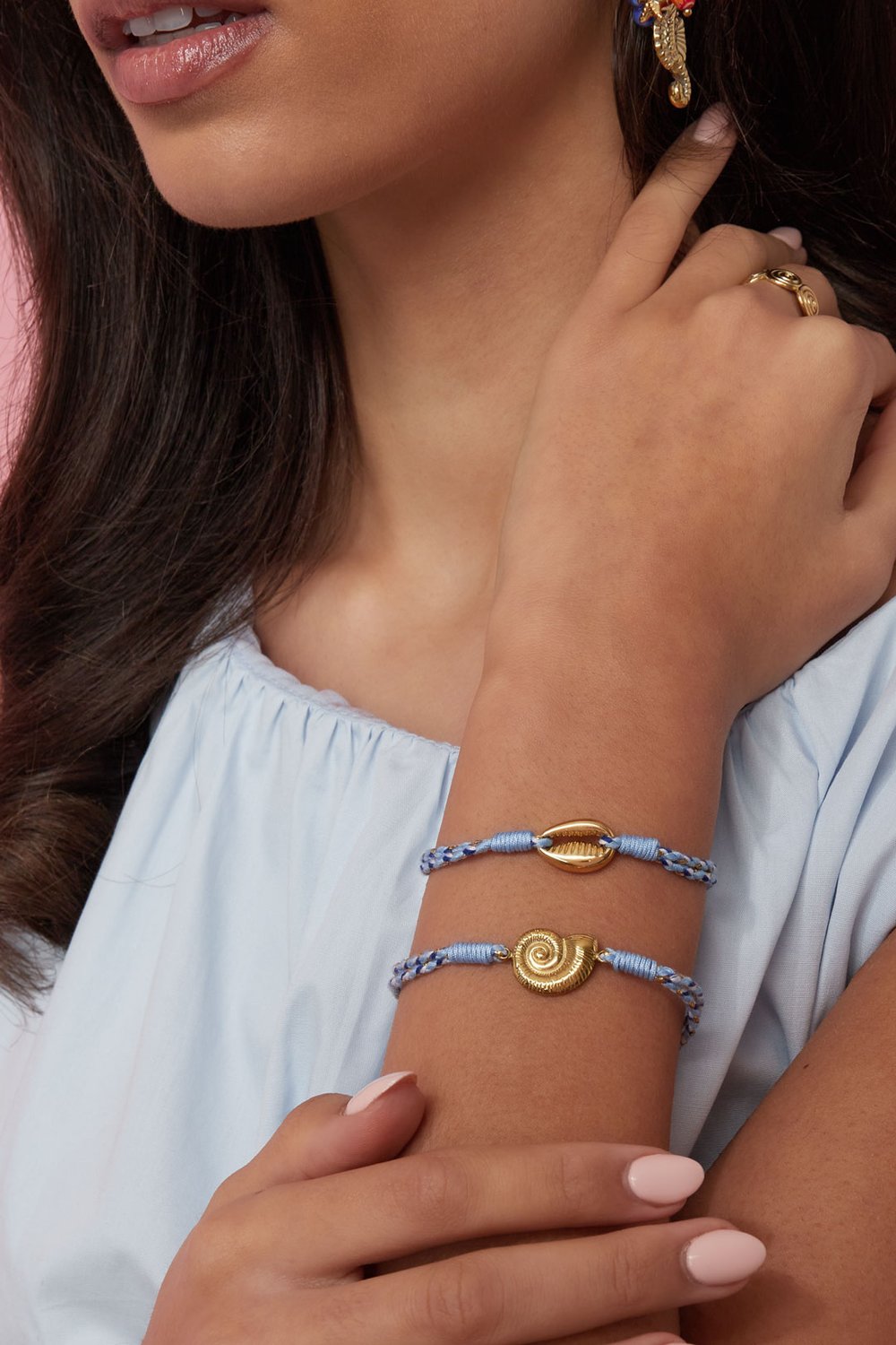 Two Playful Rope Motif bracelets featuring gold shell charms on braided blue and white cord, worn on a wrist.