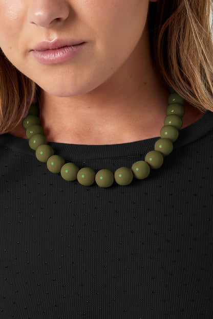 Close-up of model wearing olive green chunky bead necklace layered with heart pendant necklace over white shirt