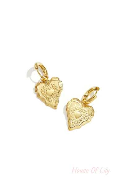Close-up of gold heart charm hoop earrings with embossed detailing on a white background