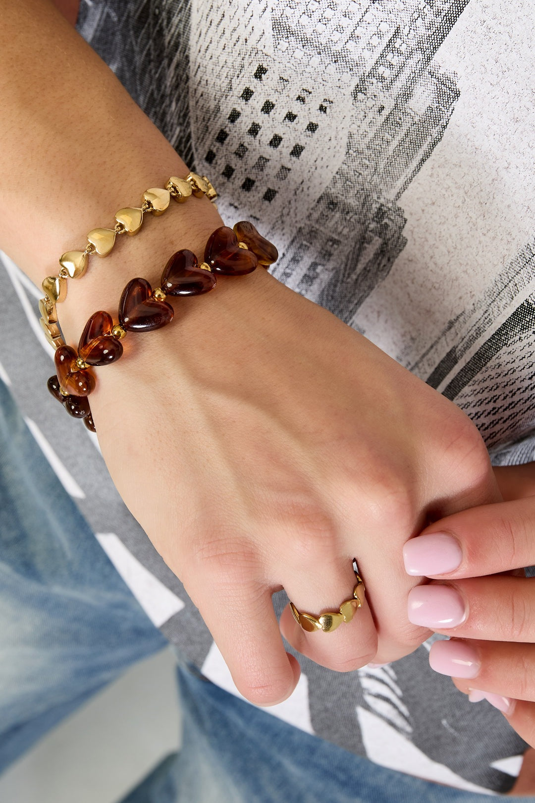 Wrist with layered heart bracelets—dark coffee brown acrylic and gold heart chain bracelet, with matching heart ring