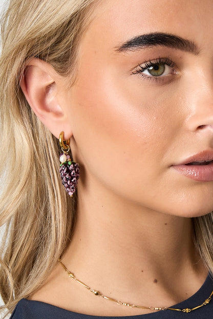 Close-up of a woman wearing a gold hoop earring with a purple grape cluster charm showcasing the playful and youthful design
