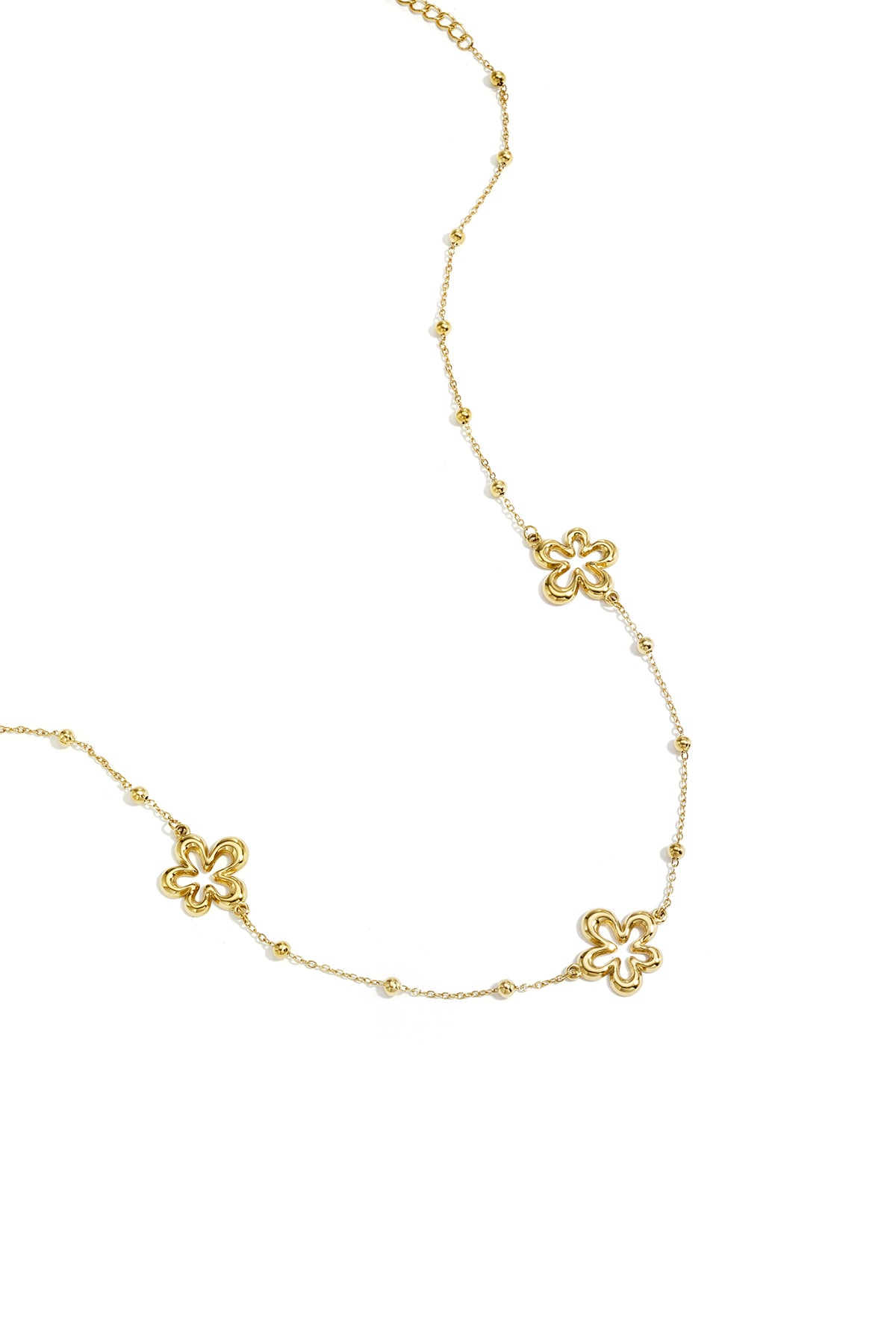 Close-up of delicate gold necklace with hollow flower charms and small bead accents on white background