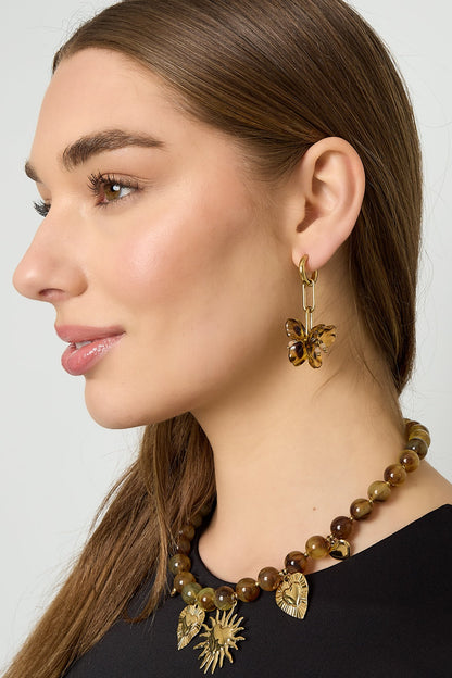 Model wearing gold-tone drop earrings featuring amber acrylic flower pendants and a matching necklace with gold charms