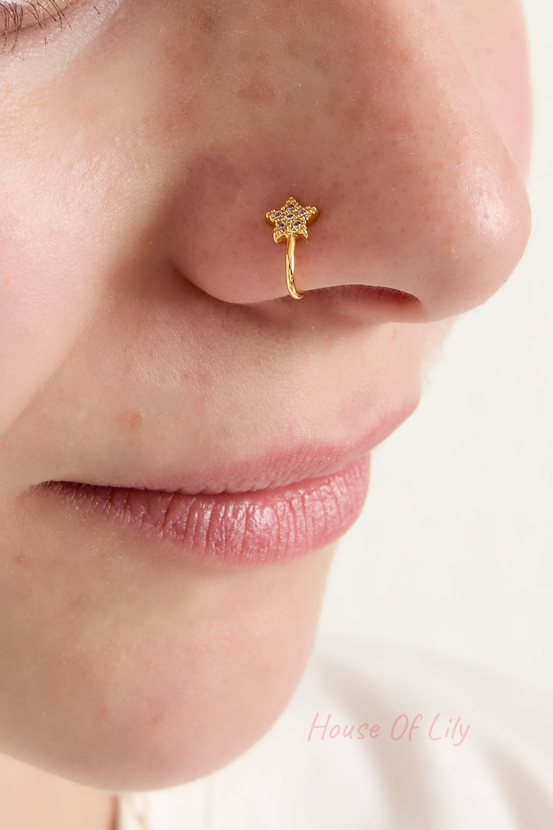 Close-up of woman's nose adorned with gold star nose cuff showing a soft smile