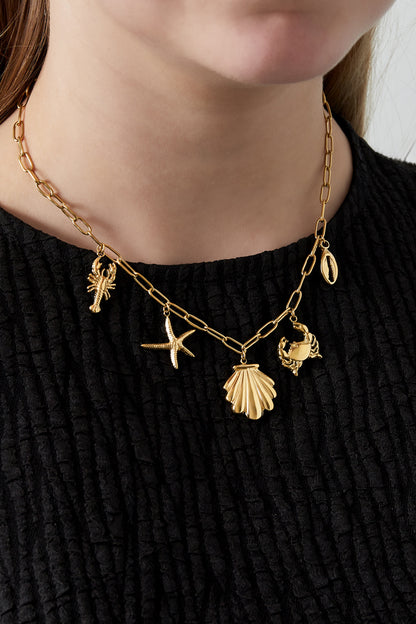 Close-up of a woman wearing the gold seaside charm necklace over a black textured top