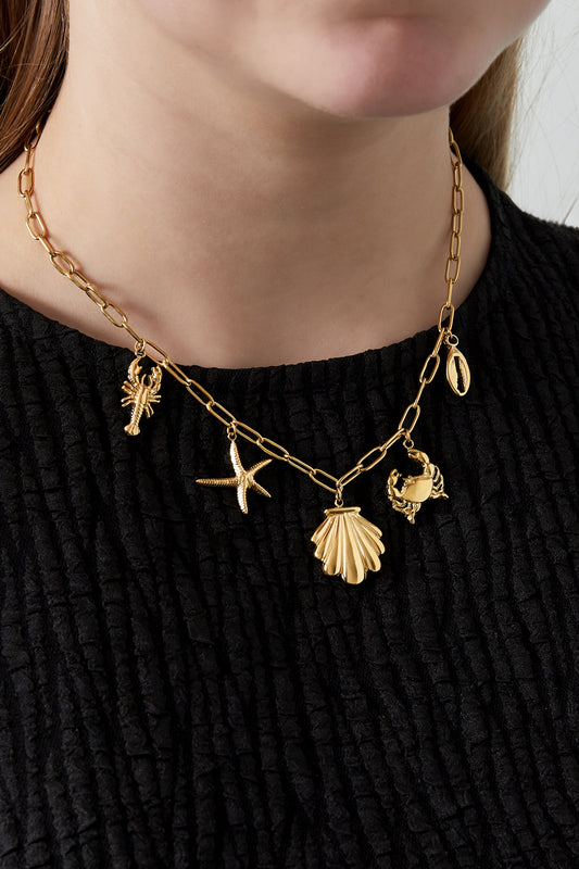 Close-up of a woman wearing the gold seaside charm necklace over a black textured top
