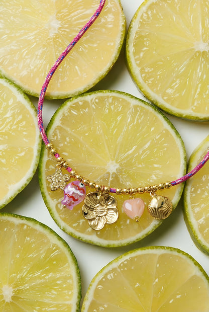 Close-up of colorful charm rope necklace resting on sliced yellow limes showing details of gold and enamel charms
