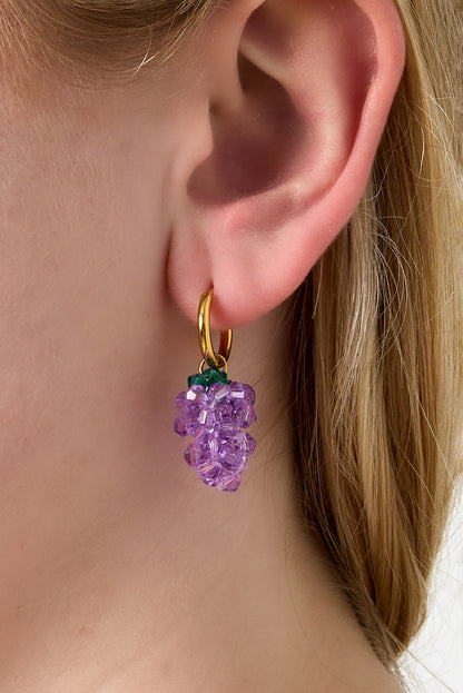Model wearing gold hoop earrings featuring playful purple grape bead dangles.