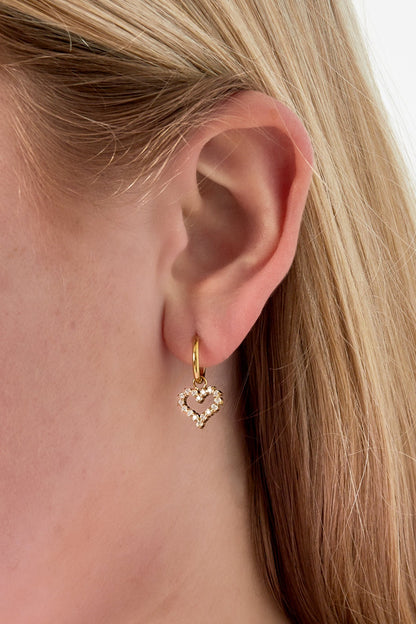 Close-up of a woman's ear wearing gold-tone hoop earring with a heart-shaped rhinestone charm