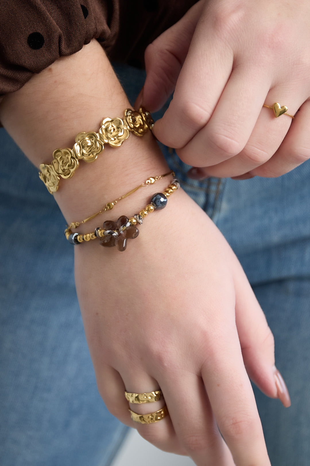 Woman's wrist wearing layered bracelets including a golden floral bracelet and a brown flower beaded bracelet